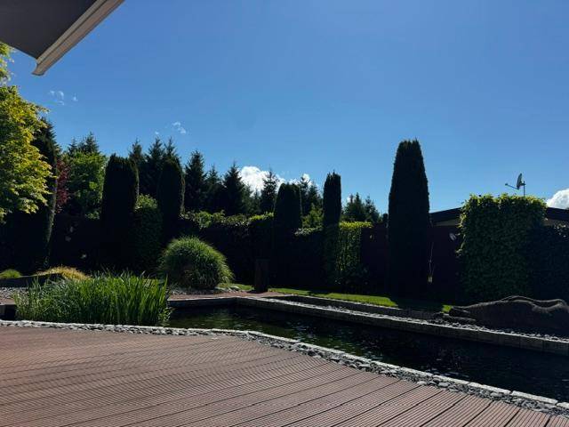 Sonnige Holzterrasse mit Blick auf einen idyllischen Teich und den üppig bepflanzten Gartenbereich.