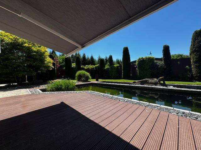 Geräumige Holzterrasse mit ausfahrbarer Markise, Teich und Blick in den gepflegten Garten.