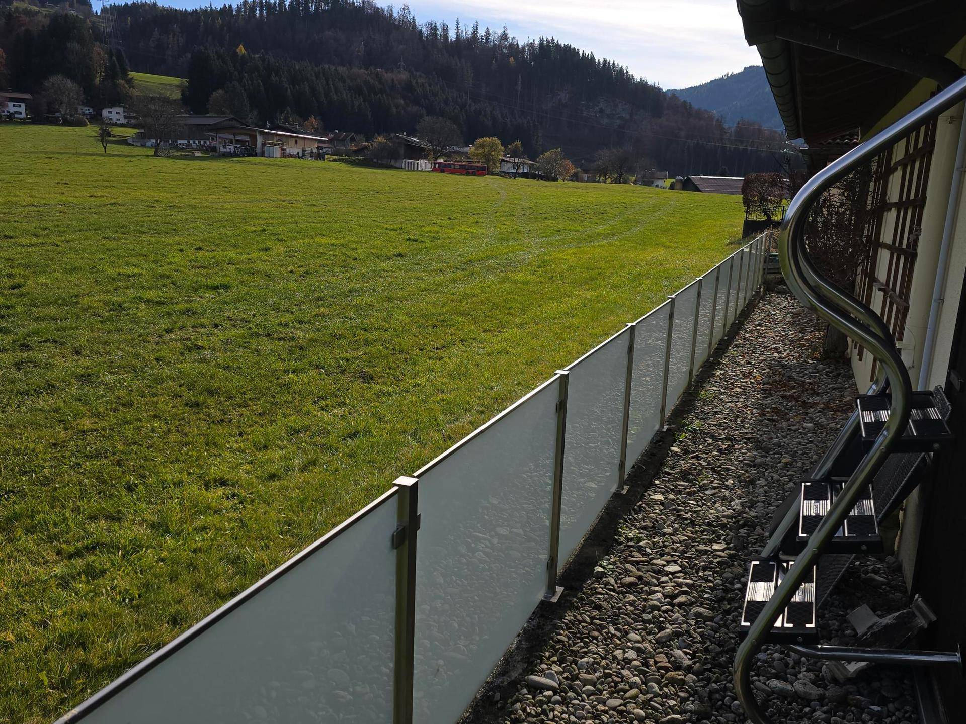 Gartenbereich mit moderner Glasabtrennung, Kiesstreifen und Panoramablick auf die Natur.