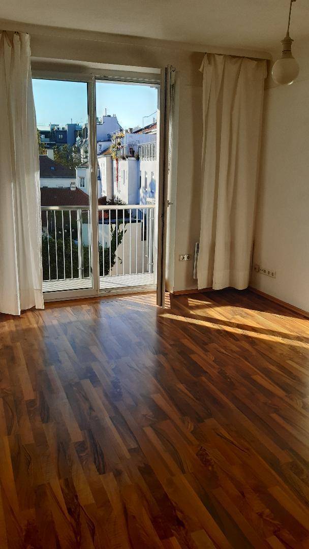 Heller Raum mit Laminatboden und großen Balkontüren, durch die viel Sonnenlicht einfällt.