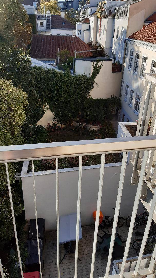 Blick von einem Balkon in einen begrünten Innenhof mit Bäumen und Abstellmöglichkeiten.