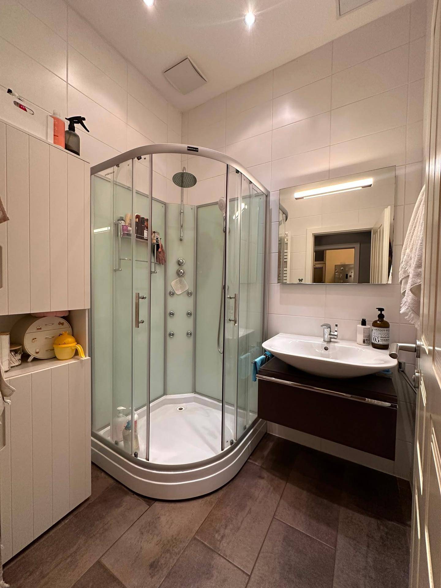 Modernes Badezimmer mit Eckdusche, Waschbecken mit Unterschrank und weißen Fliesen.