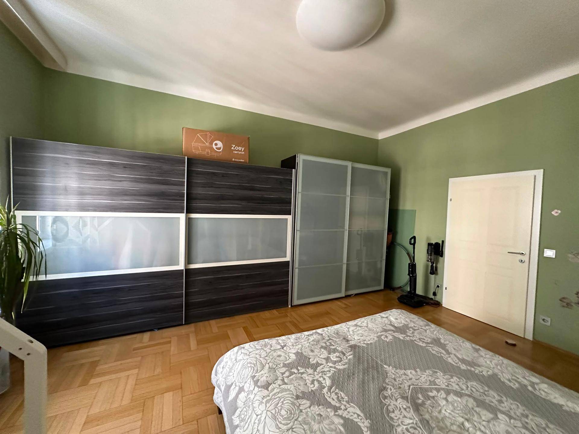 Schlafzimmer mit großem Schiebetürenschrank, grünen Wänden und Parkettboden.