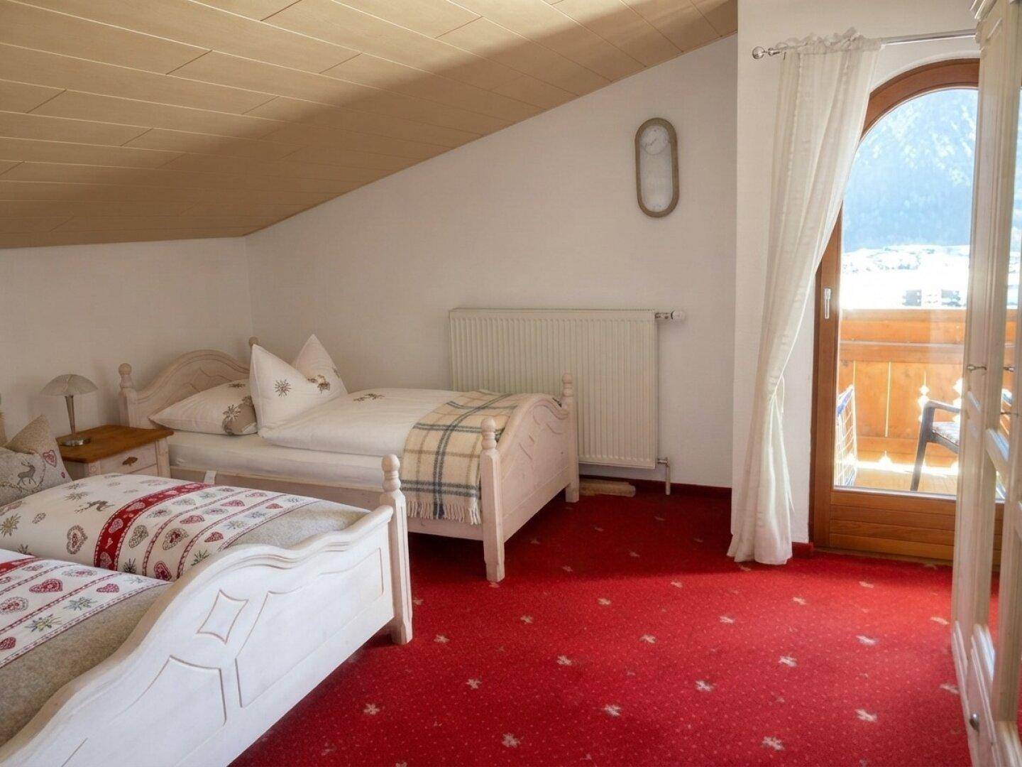 Gemütliches Schlafzimmer im Dachgeschoss mit zwei Betten, rotem Teppich und Balkonzugang.