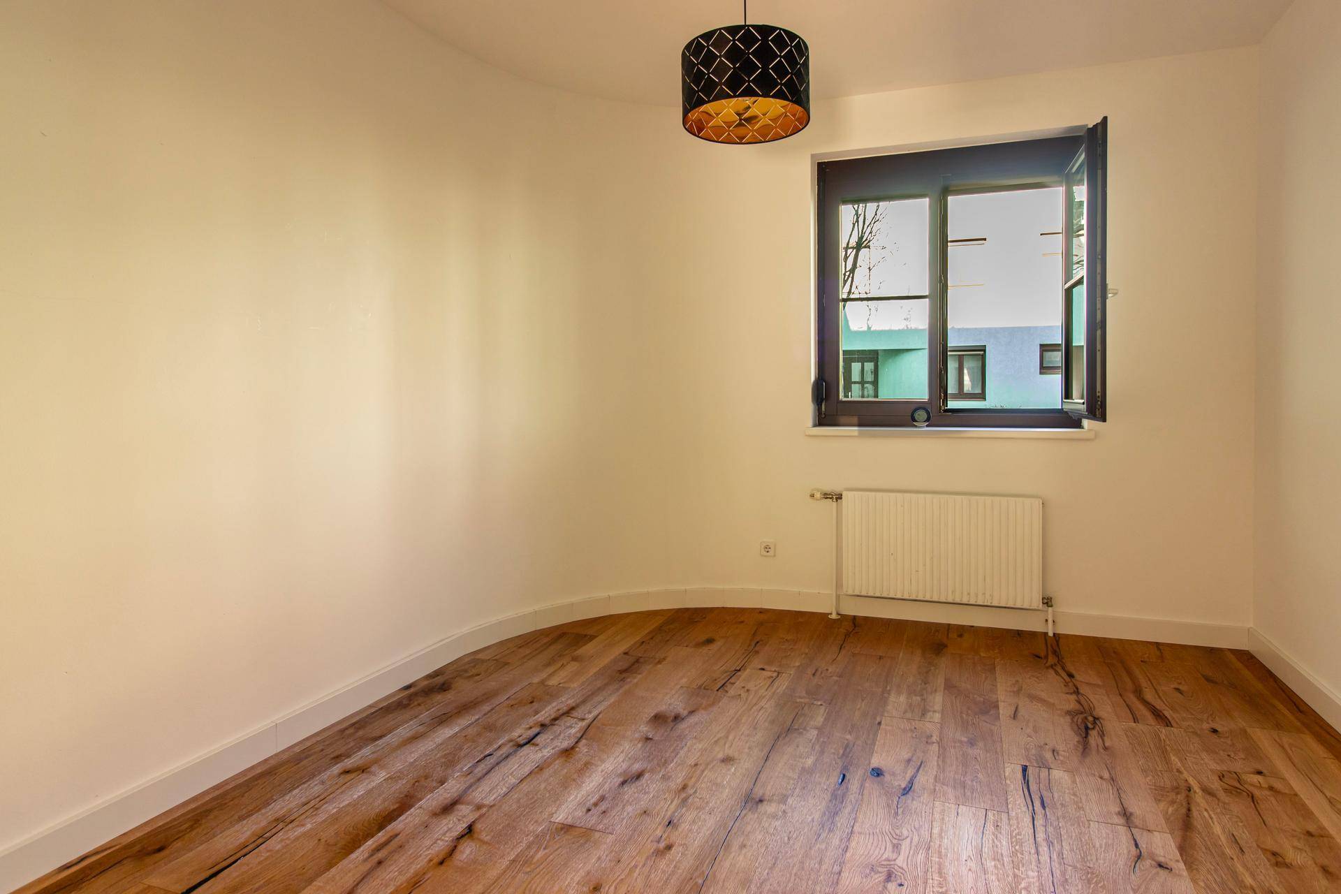 Gemütliches Schlafzimmer mit Holzboden und einem Fenster mit Blick nach draußen auf die Umgebung.