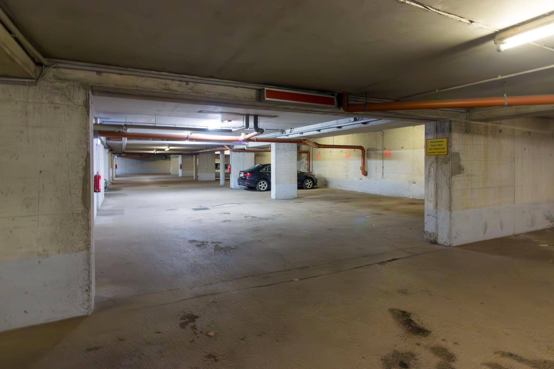 Tiefgarage mit Betonwänden und -boden, bietet Parkplätze für mehrere Fahrzeuge.
