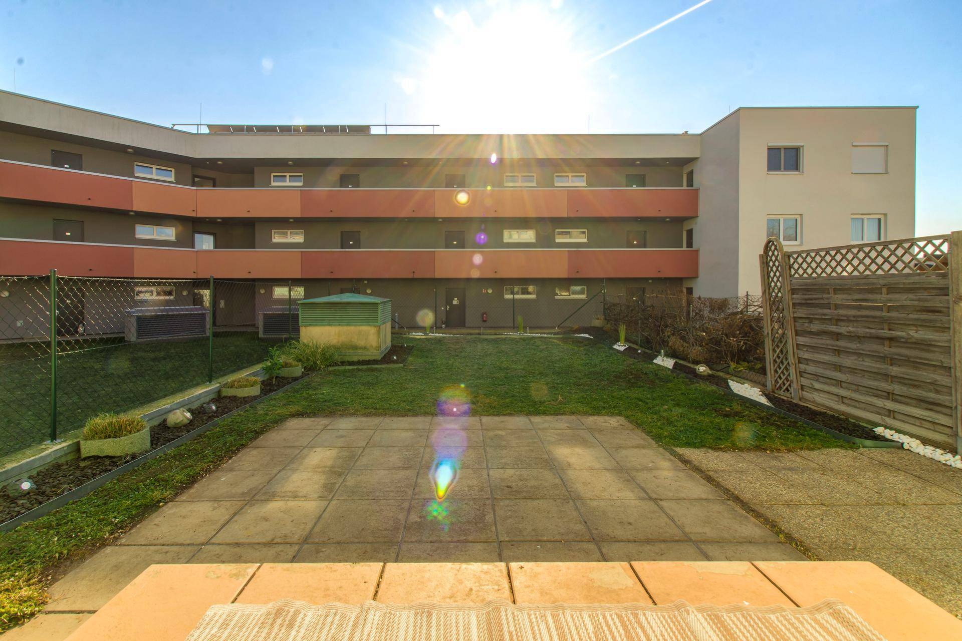 Sonniger Gartenbereich mit gepflasterter Terrasse und Blick auf das Mehrfamilienhaus.