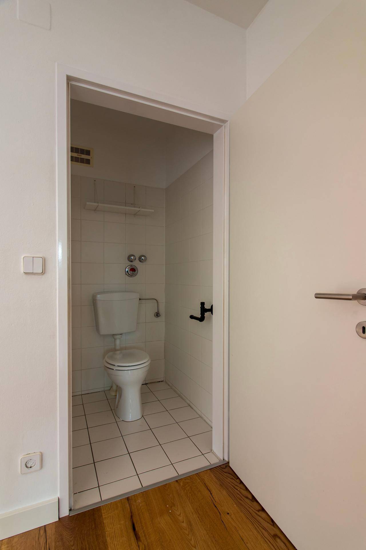 Separate Toilette mit weißen Fliesen und einem kleinen Fenster für natürliche Belüftung.
