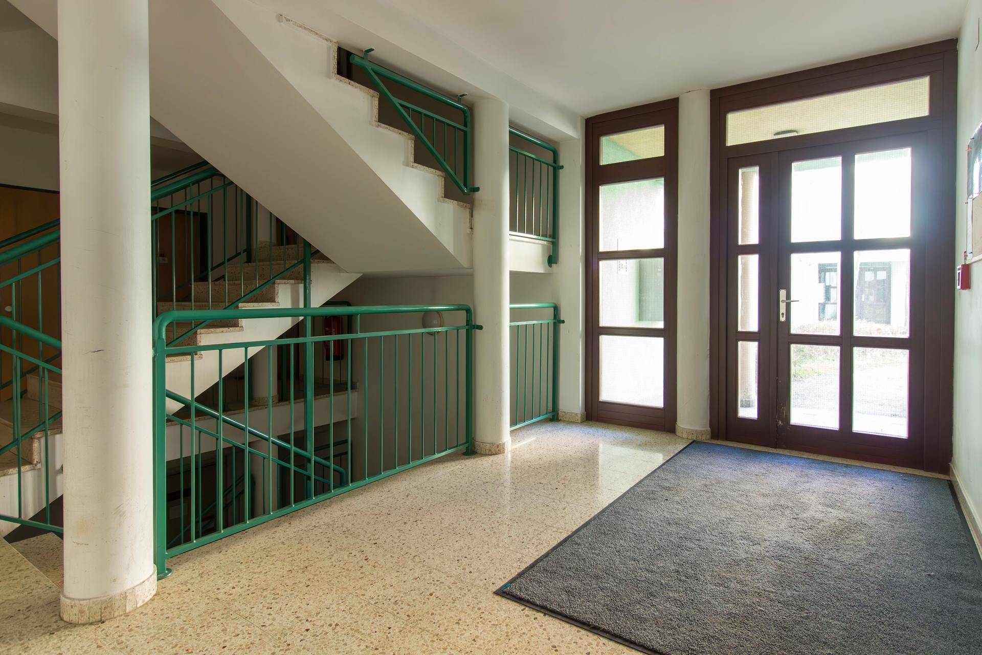 Eingangsbereich eines Mehrfamilienhauses mit Treppenhaus und Terrazzoboden.