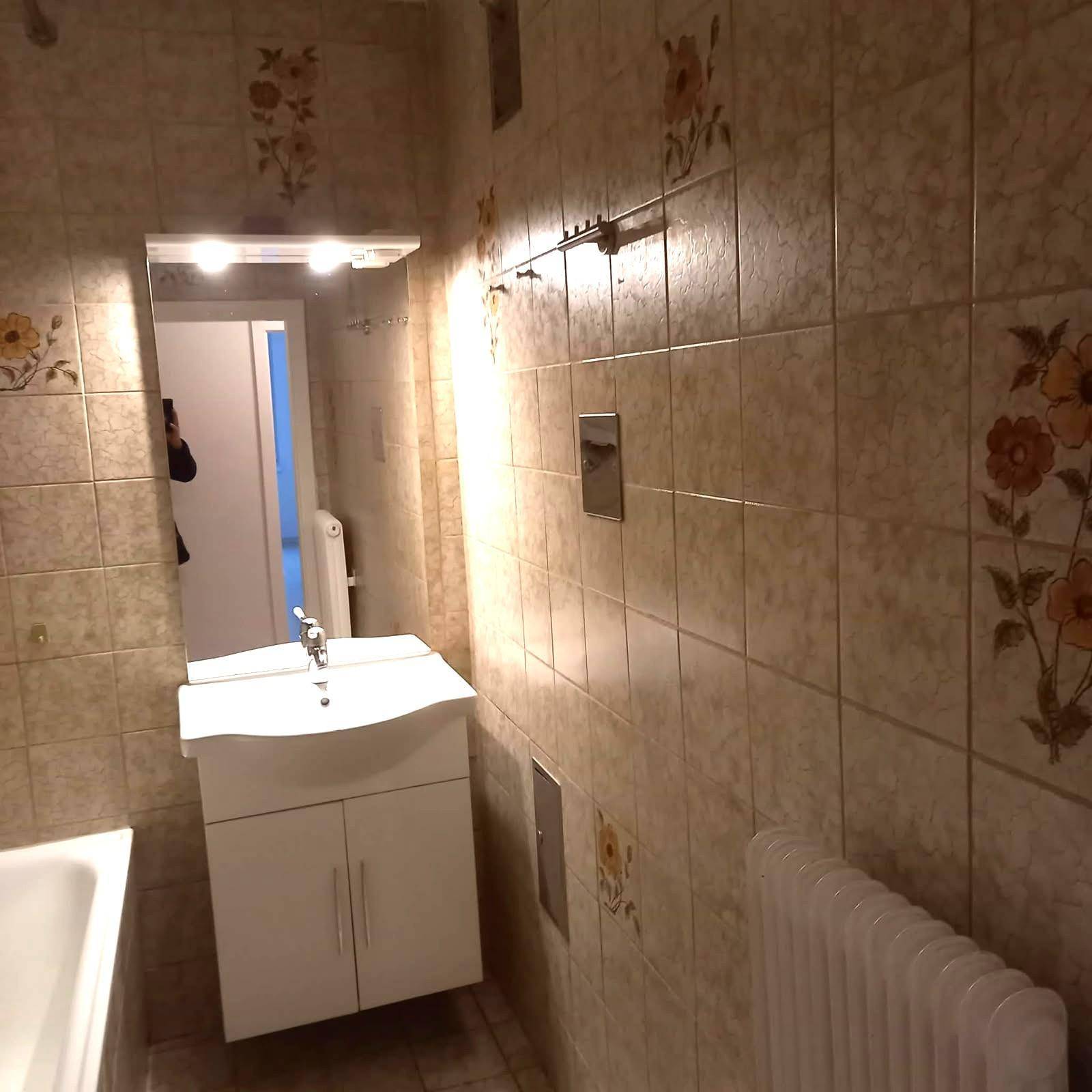 Badezimmer mit floralen Fliesen, Waschbecken, Spiegelschrank und Heizkörper.