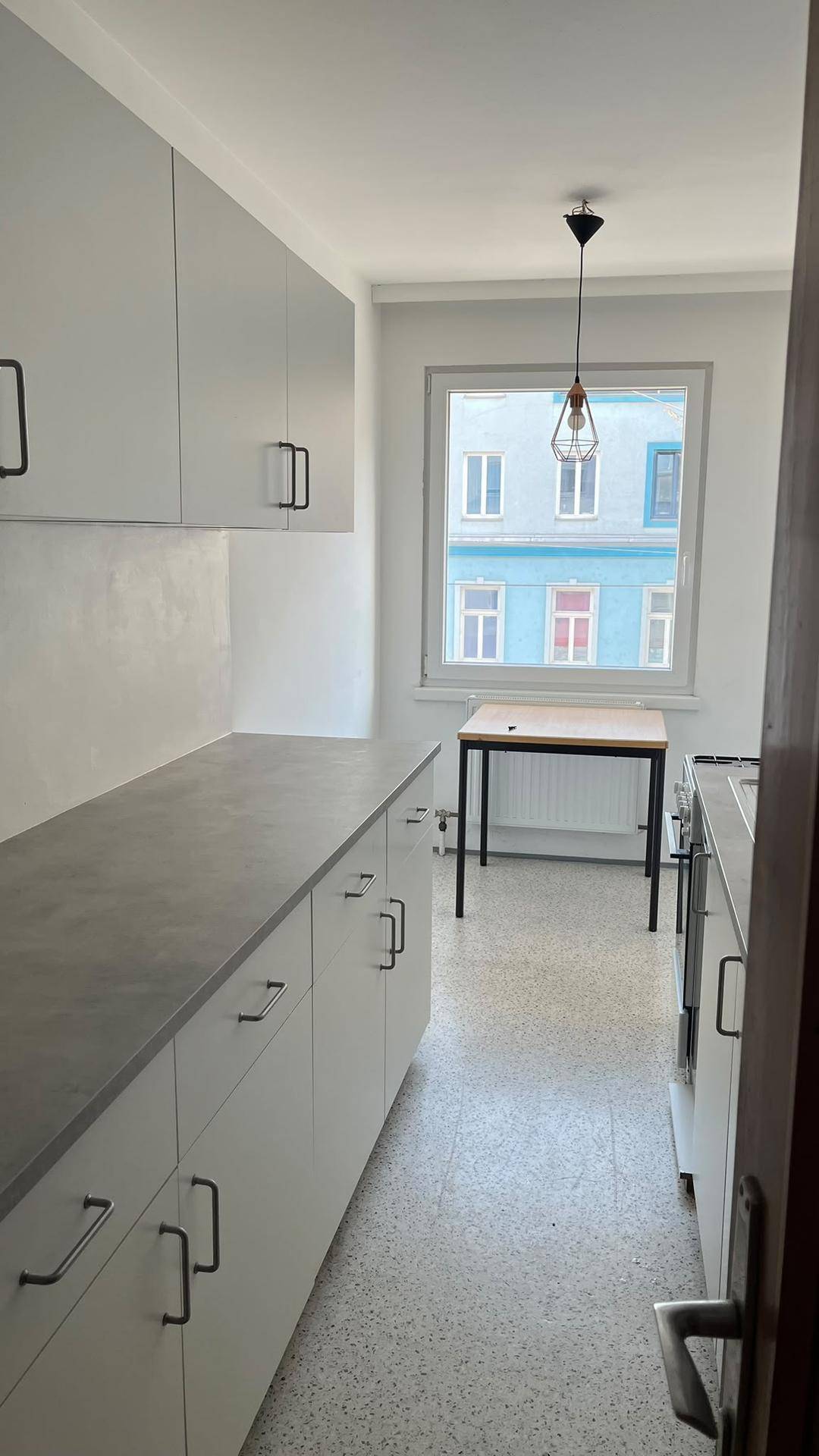 Moderne Küche mit grauen Schränken, Arbeitsplatte und einem Fenster mit Blick auf die Stadt.