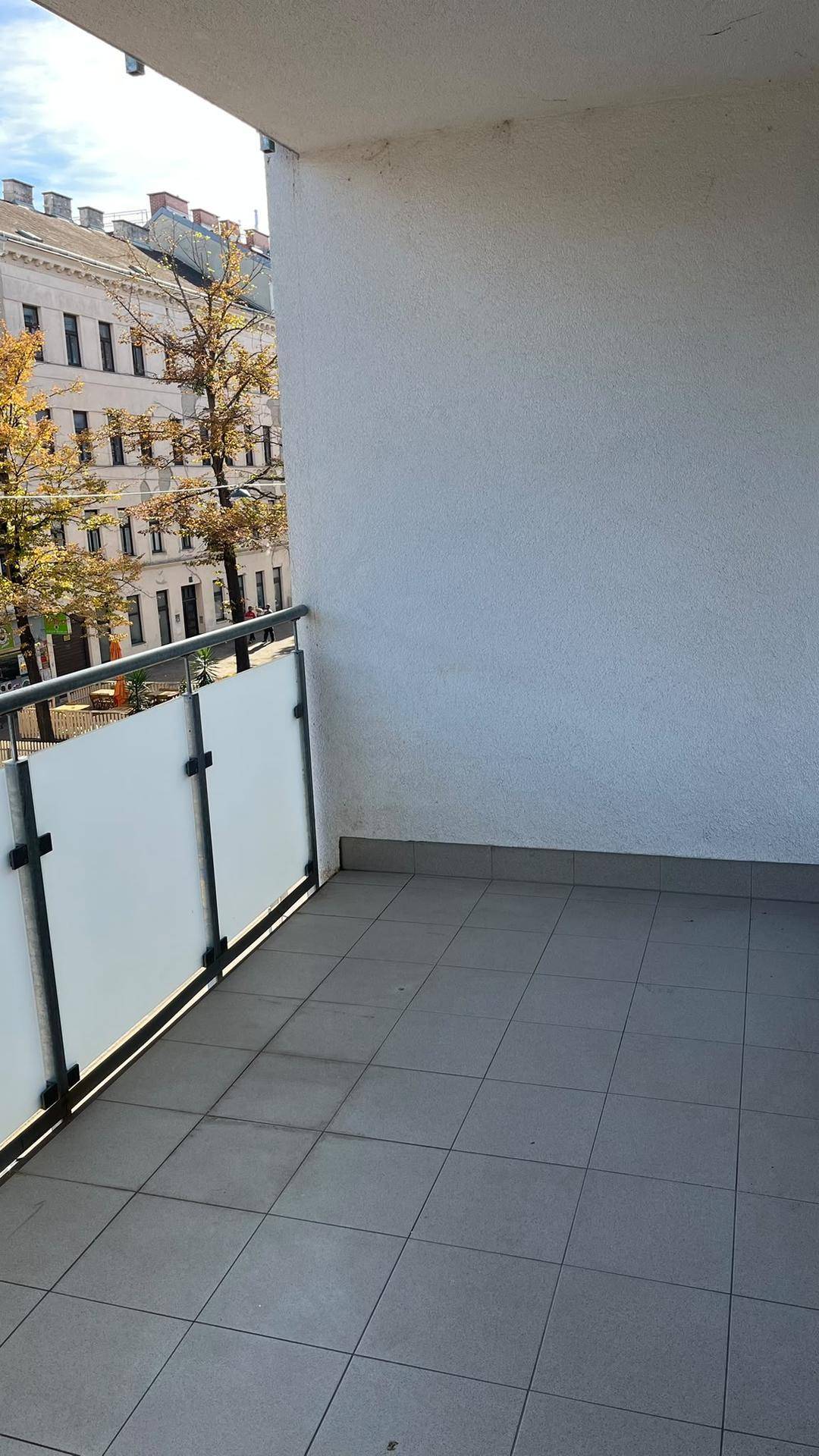 Balkon mit grauen Fliesen und Blick auf die umliegenden Gebäude und die Straße.
