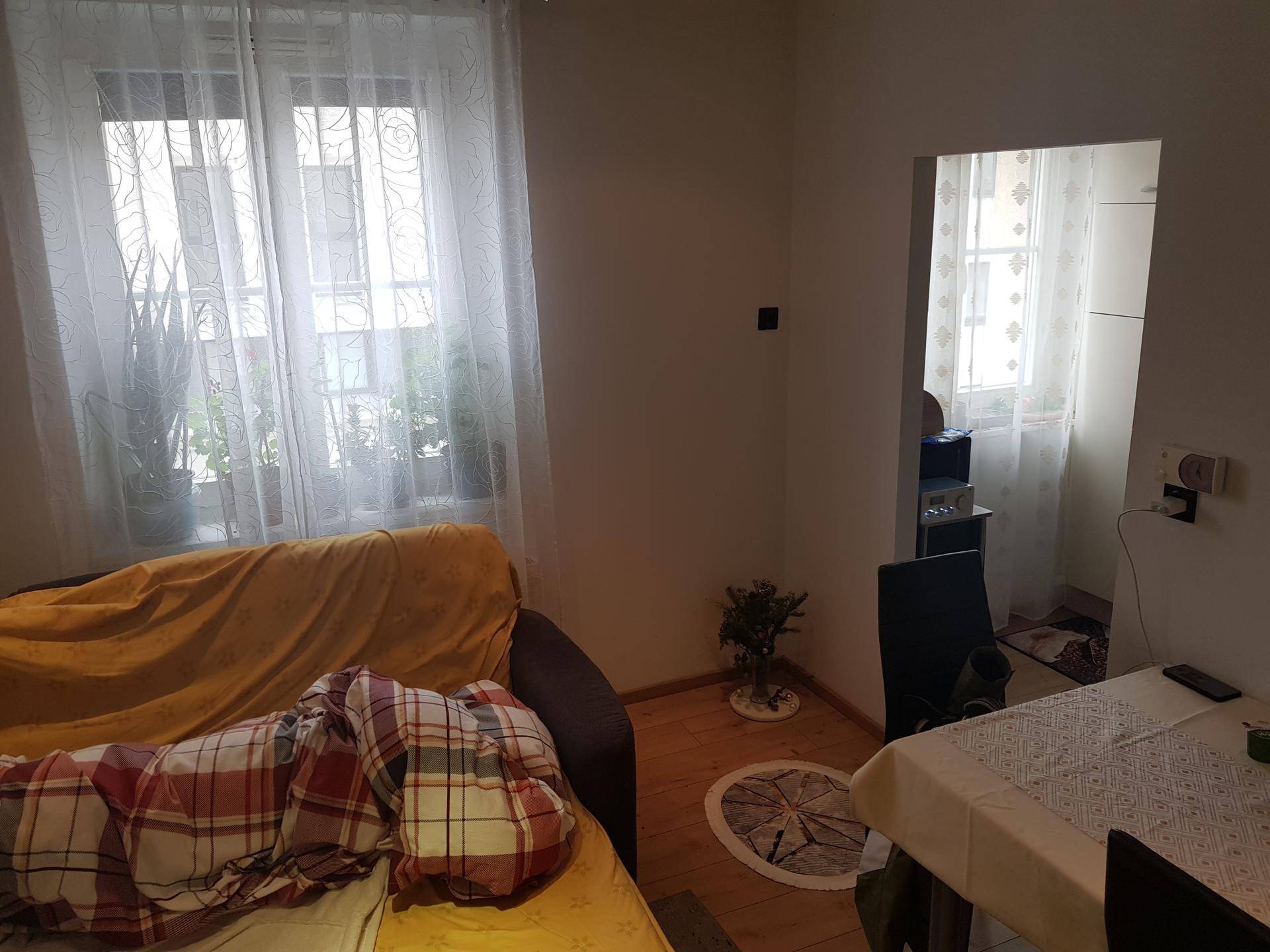 Gemütlicher Wohn- und Essbereich mit Sofa, Esstisch und zwei Fenstern mit Vorhängen.