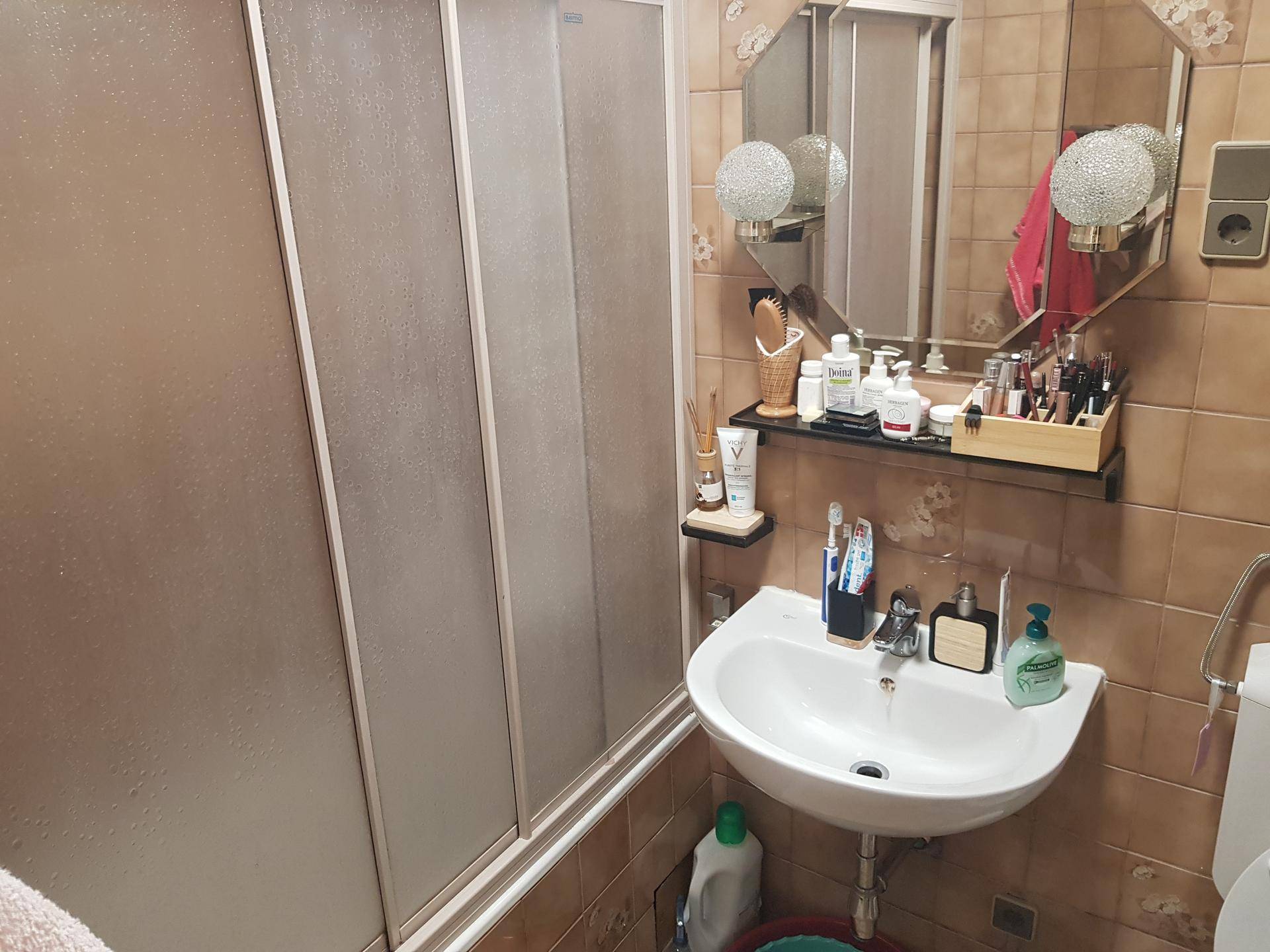 Badezimmer mit Duschkabine, Waschbecken und braunen Fliesen an den Wänden.