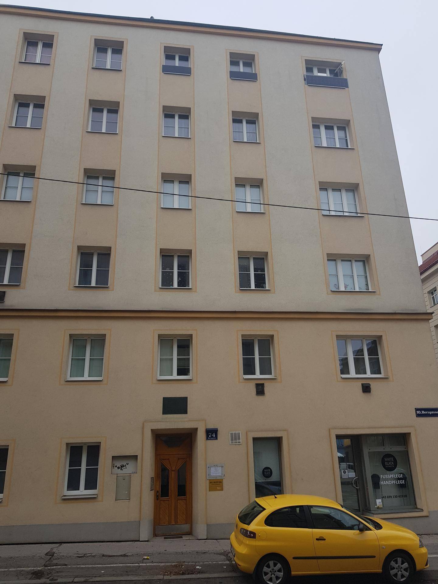 Fassade eines Wohngebäudes mit Eingangstür und Fenstern an einer städtischen Straße.