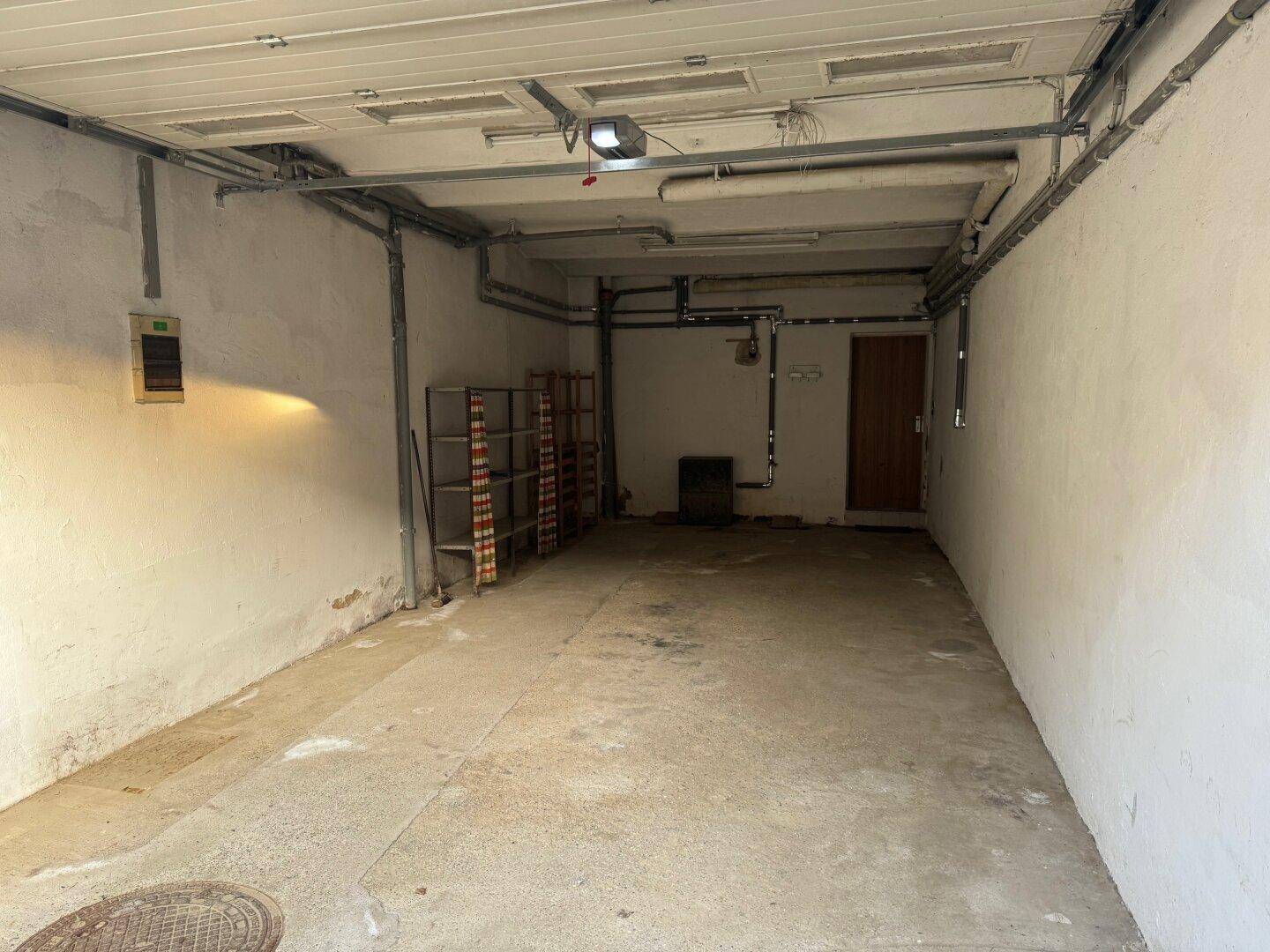 Langer Garagenraum mit Betonboden, weißen Wänden und sichtbaren Installationen, bietet viel Stauraum.