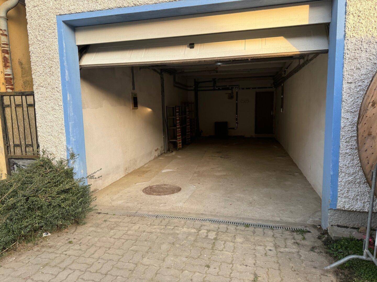 Geräumige Garage mit Betonboden und offenem Garagentor, ideal für Fahrzeuge und Lagerung.