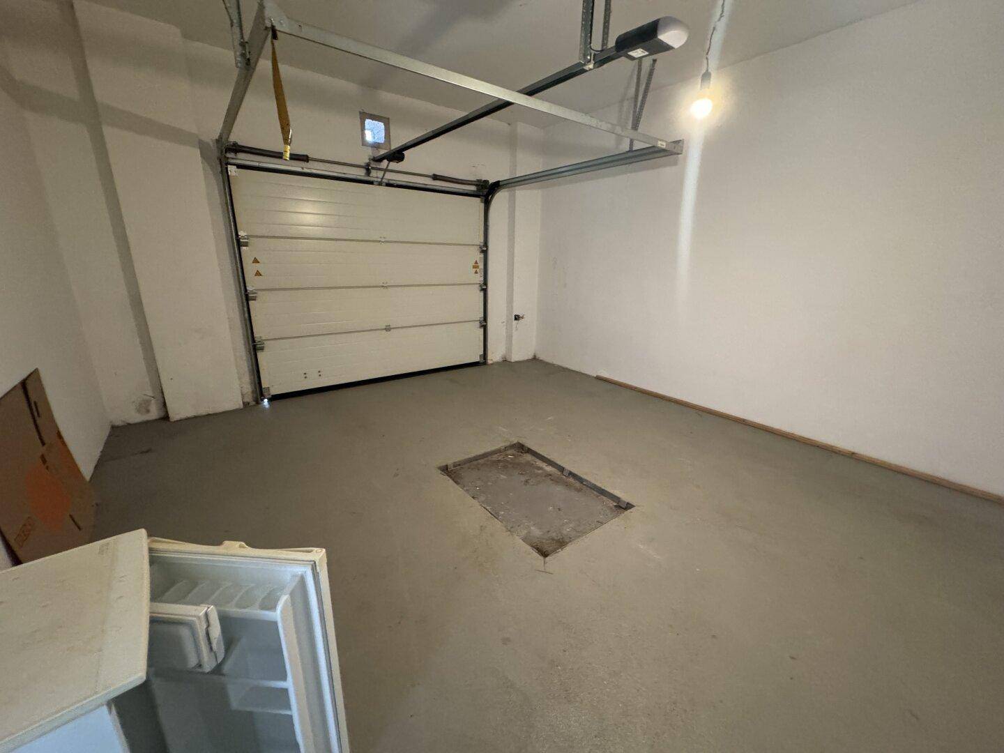 Leere Garage mit Betonboden, automatischem Tor und einer Grube in der Mitte.