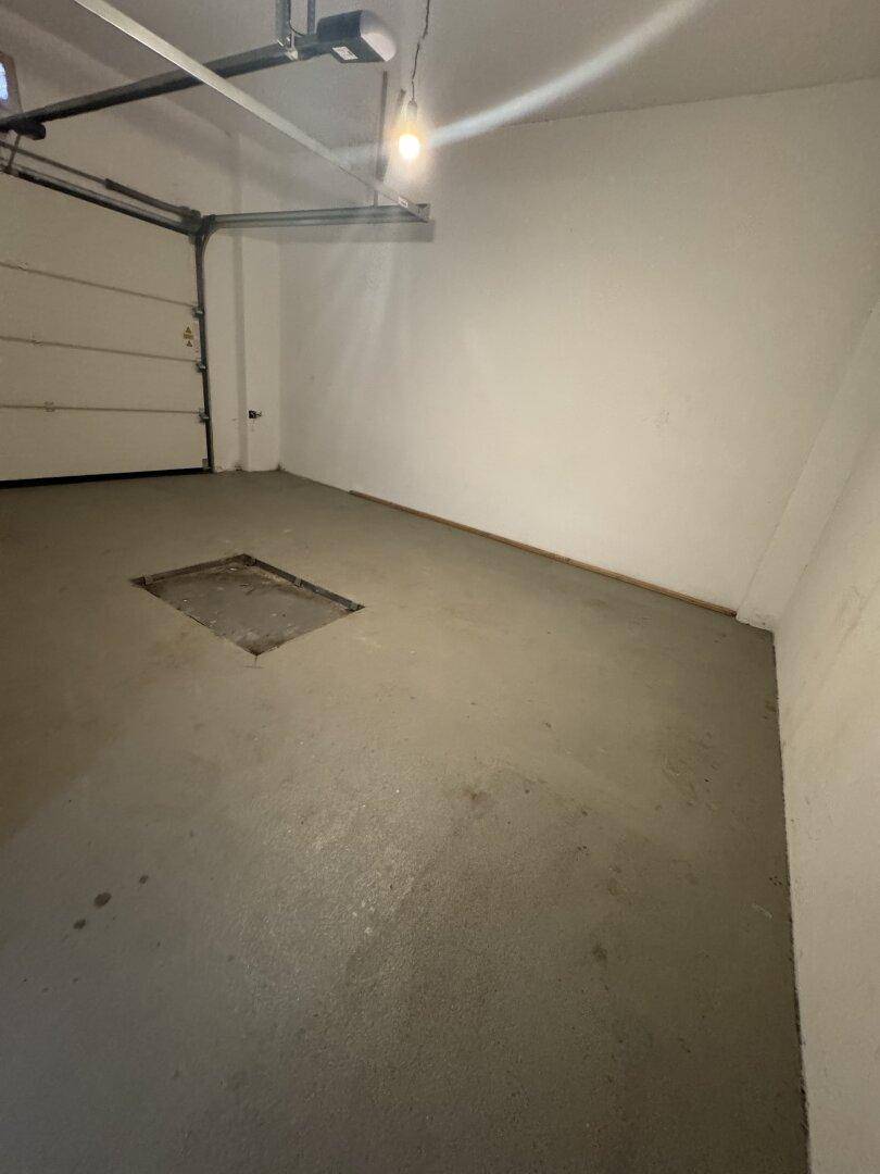 Geräumige Garage mit Betonboden und einem geöffneten automatischen Garagentor.