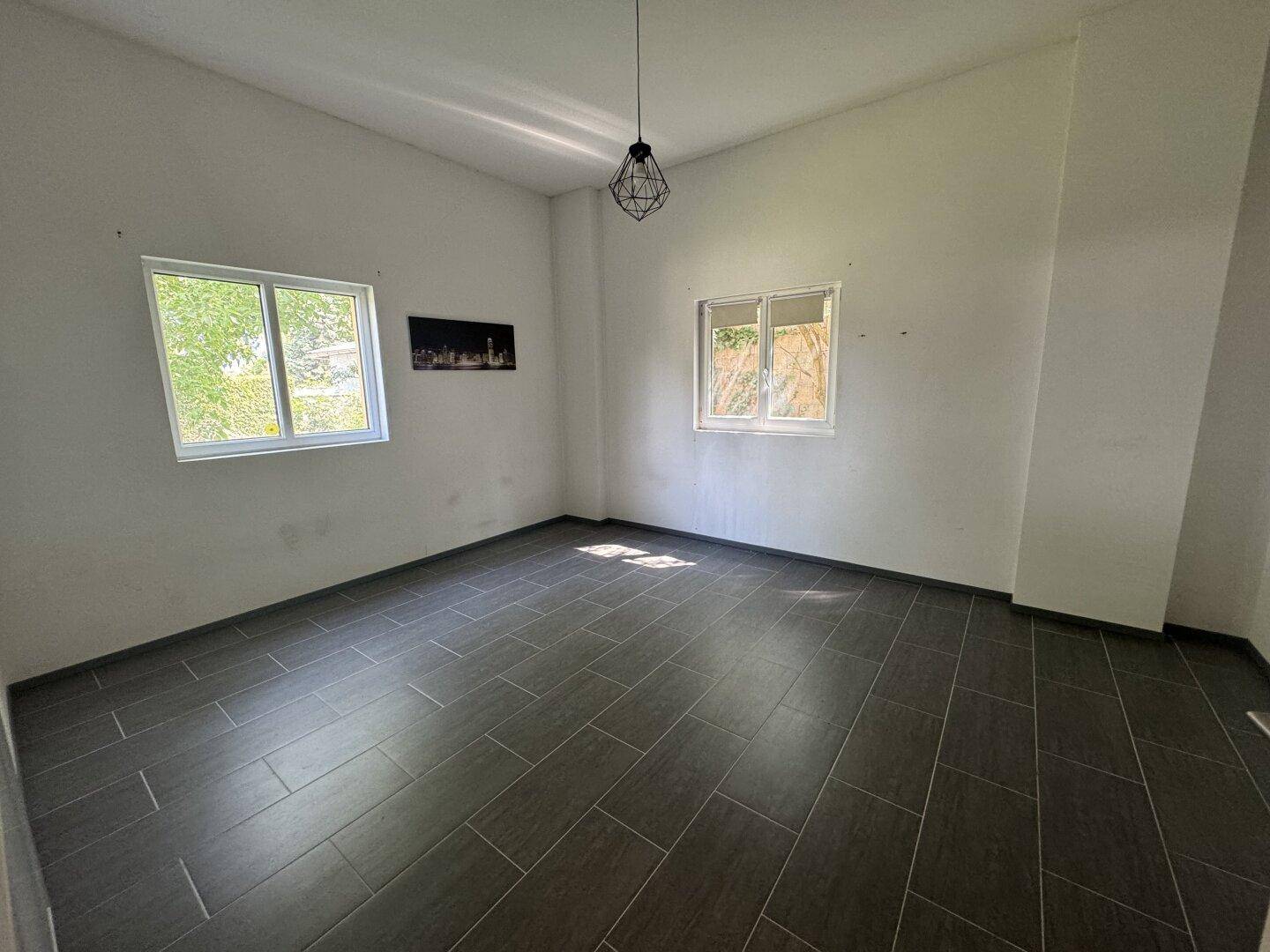 Heller Raum mit dunklen Fliesen, zwei Fenstern und einer modernen Hängelampe.