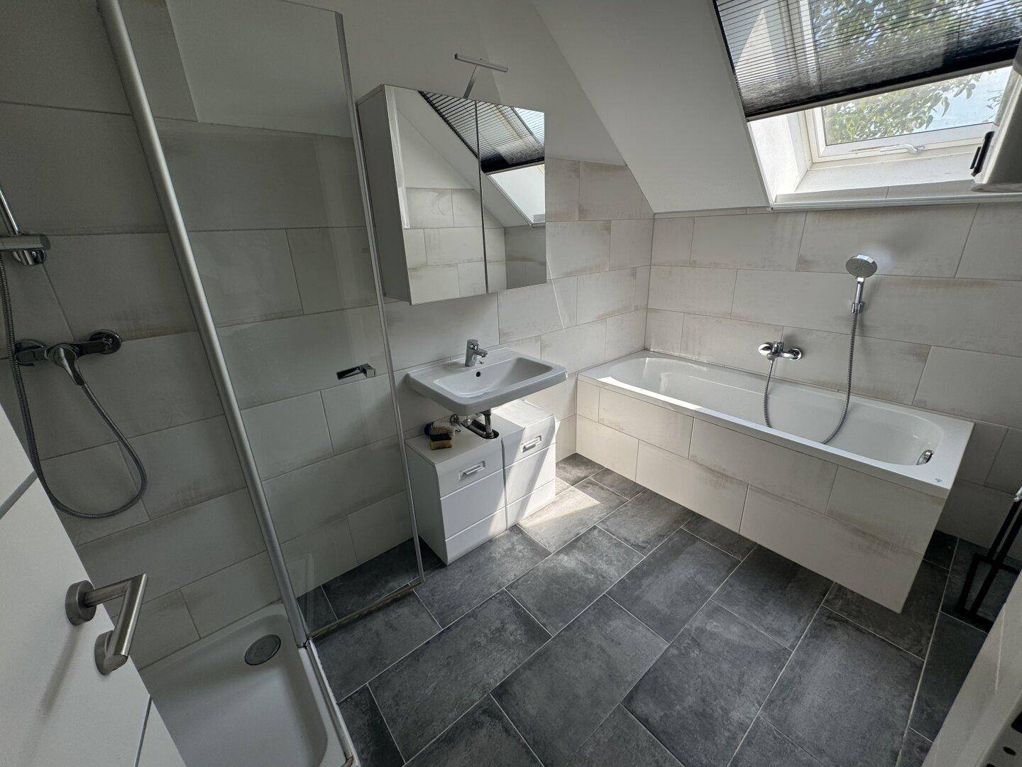 Modernes Badezimmer mit Dusche, Badewanne, Waschbecken und Dachfenster für natürliches Licht.