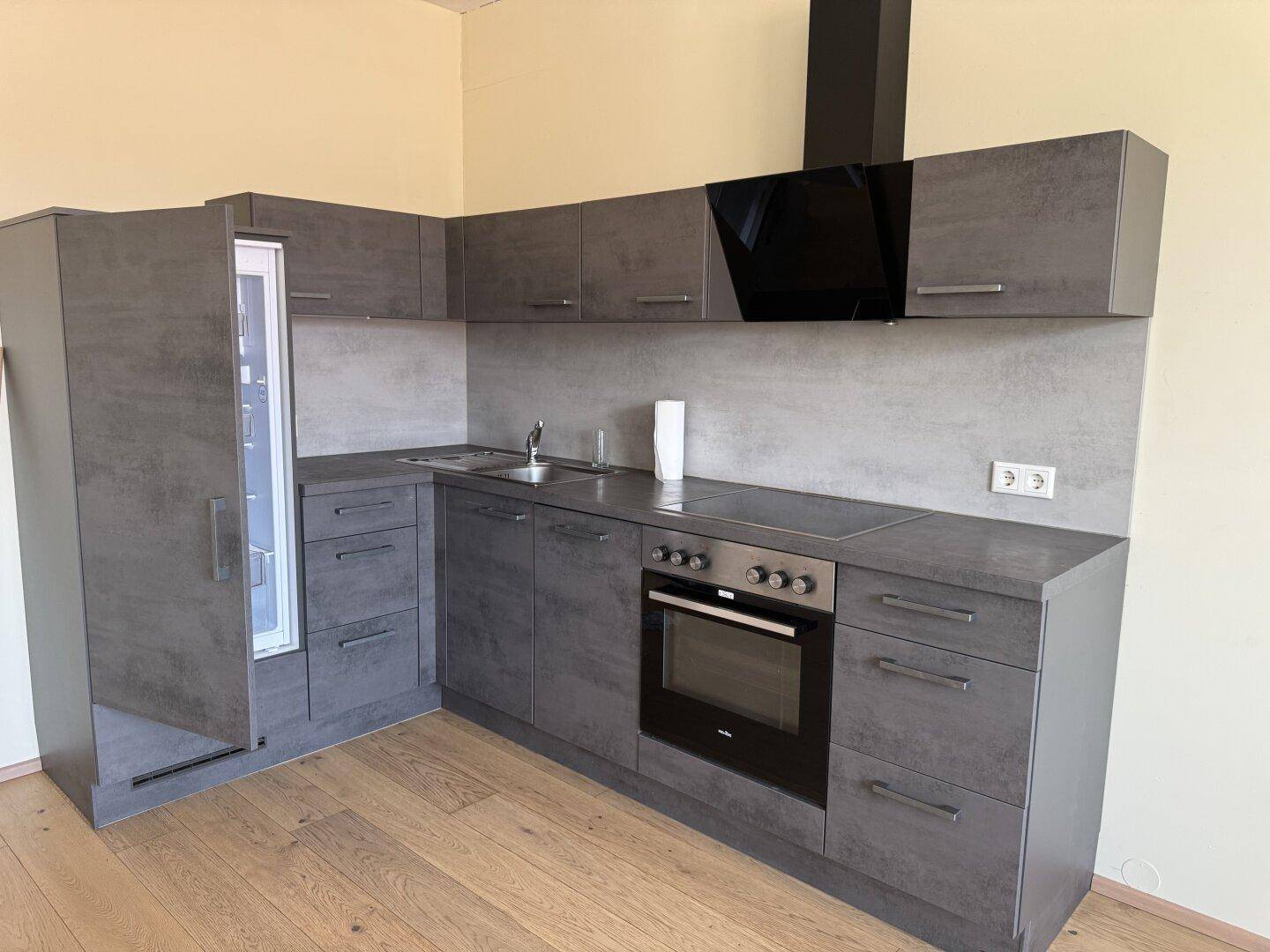 Moderne Einbauküche mit grauen Schränken, integrierten Geräten und Dunstabzugshaube.
