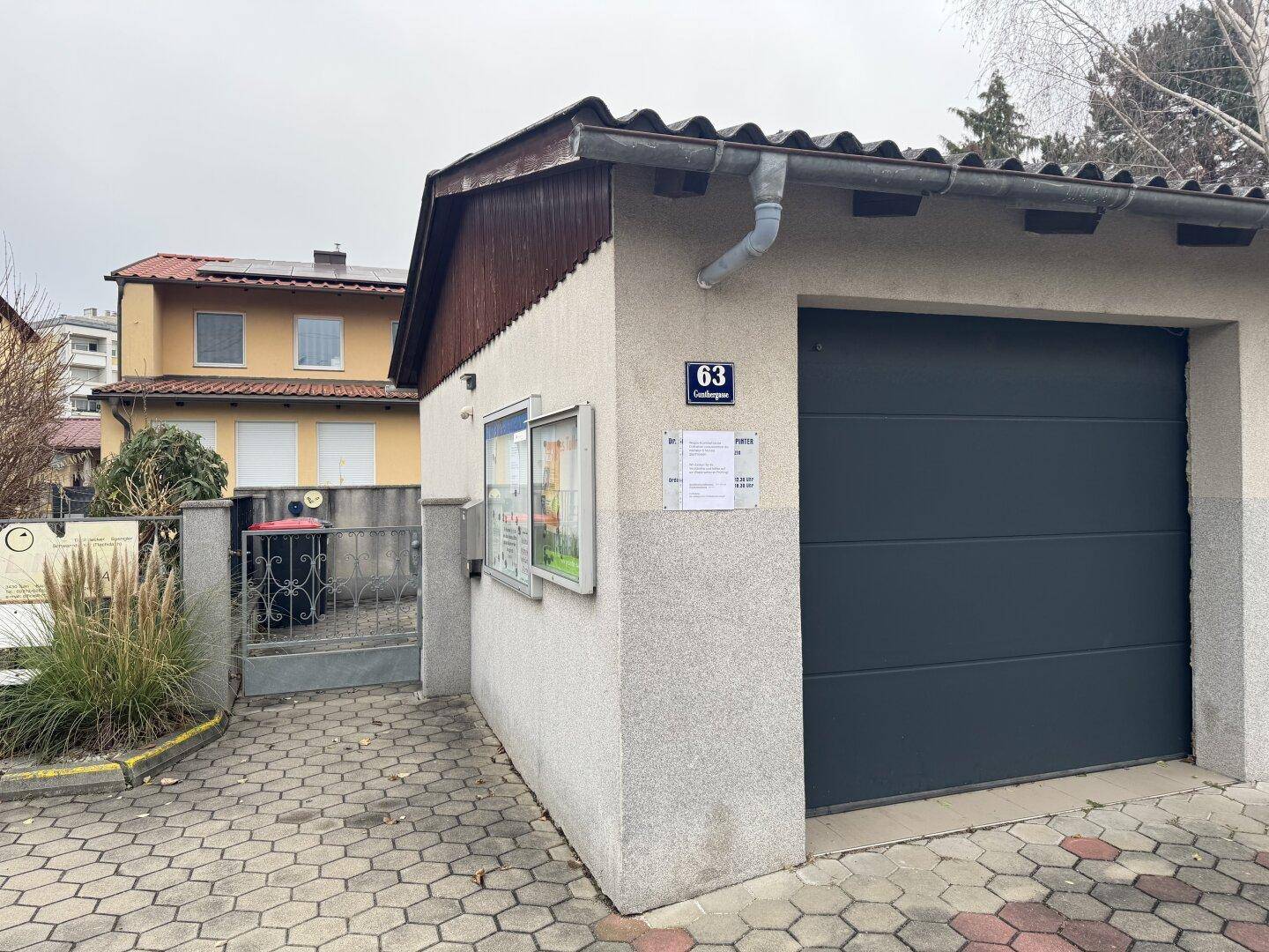 Einzelgarage mit dunklem Tor und Zufahrt, neben einem Wohngebäude gelegen.
