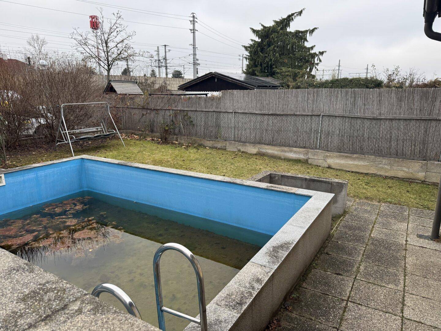 Gartenbereich mit einem leeren Swimmingpool, Rasenfläche und einem Zaun.
