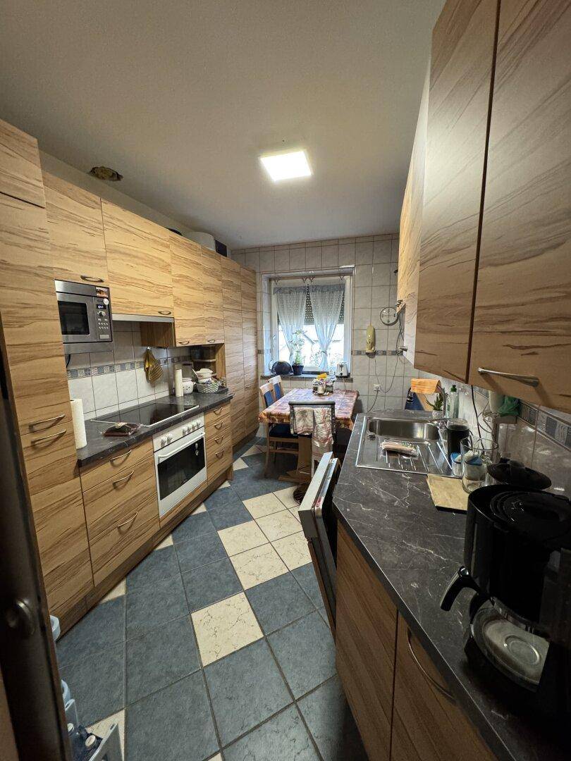 Küche mit Holzschränken, dunklen Arbeitsplatten, Einbaugeräten und Essbereich.