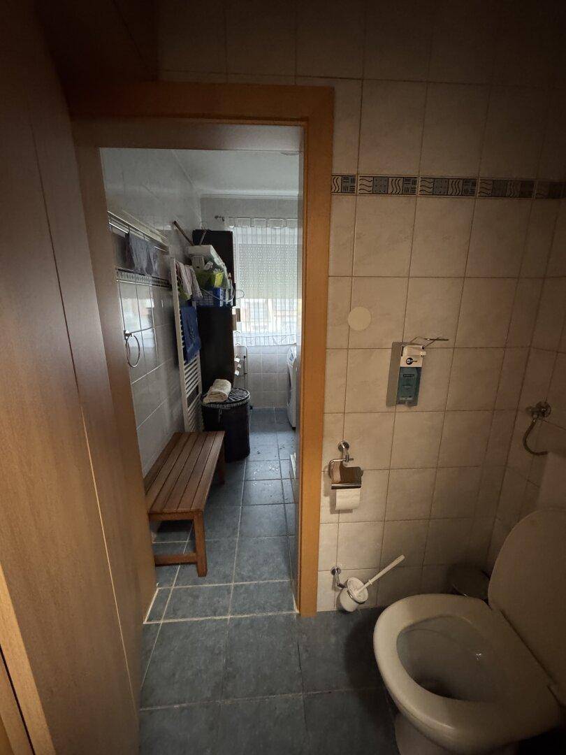 WC mit Blick in einen angrenzenden Raum, in dem eine Waschmaschine steht.