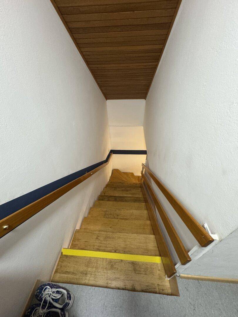 Holztreppe mit Geländer, die in ein Untergeschoss führt.