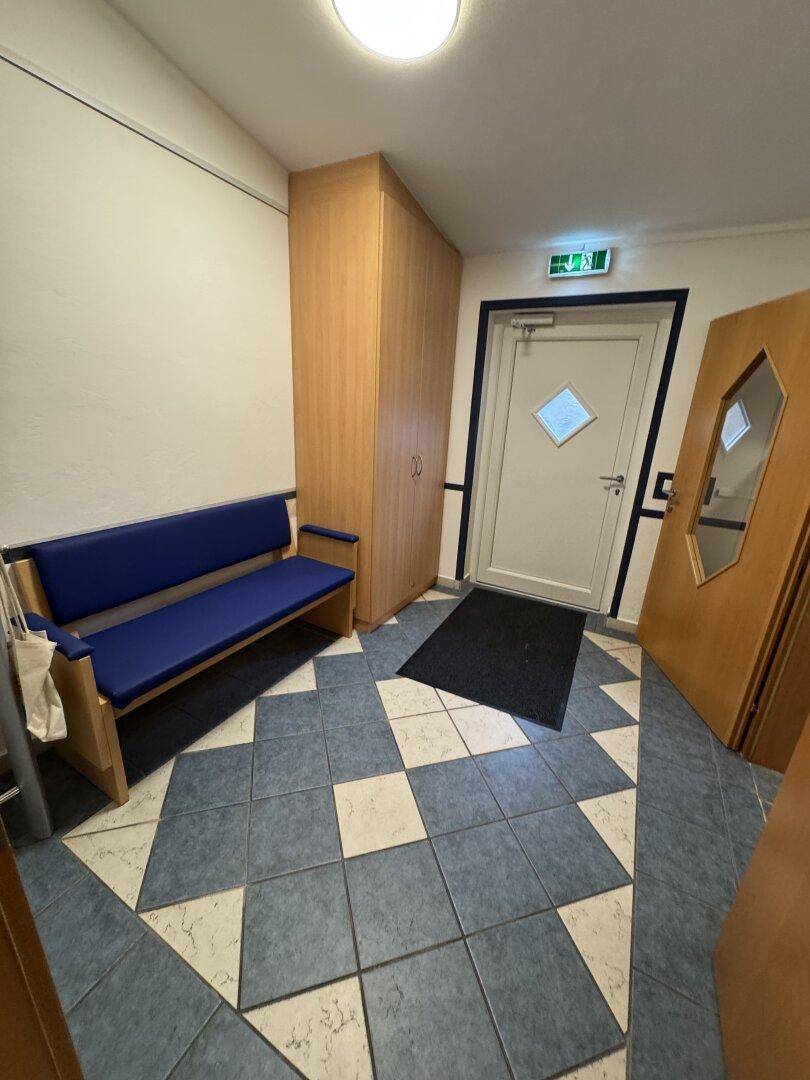 Flur mit blauer Sitzbank, Holzschrank und gemustertem Fliesenboden.