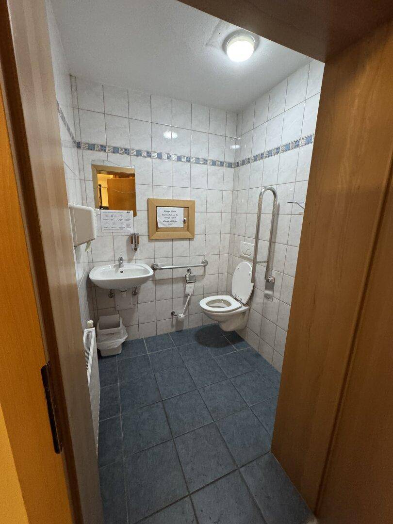 Kleines WC mit Waschbecken, Toilette und Haltegriffen für Barrierefreiheit.