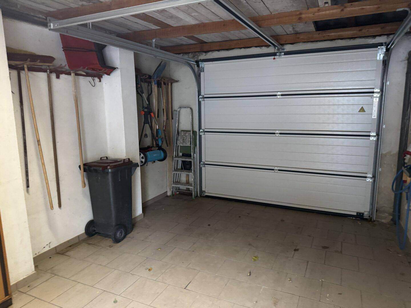 Innenansicht einer Garage mit Garagentor, Werkzeugen und Abfallbehälter.