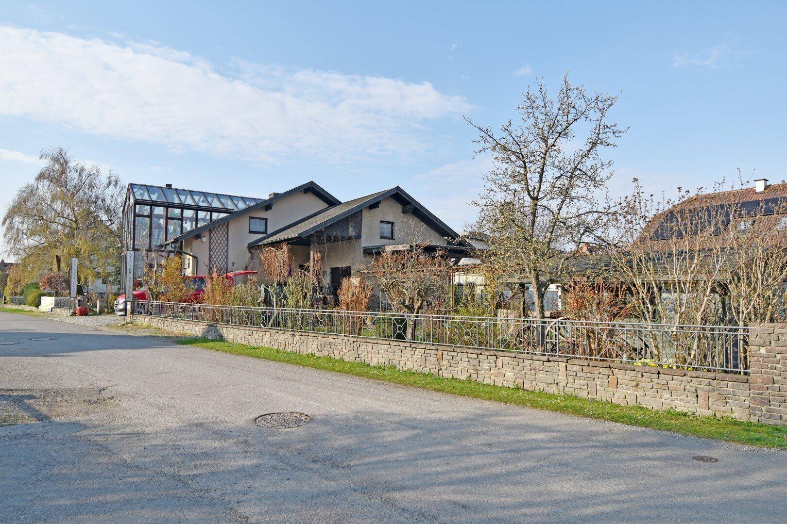 Ansicht des Hauses von der Straße mit Steinmauer und umliegenden Gebäuden.