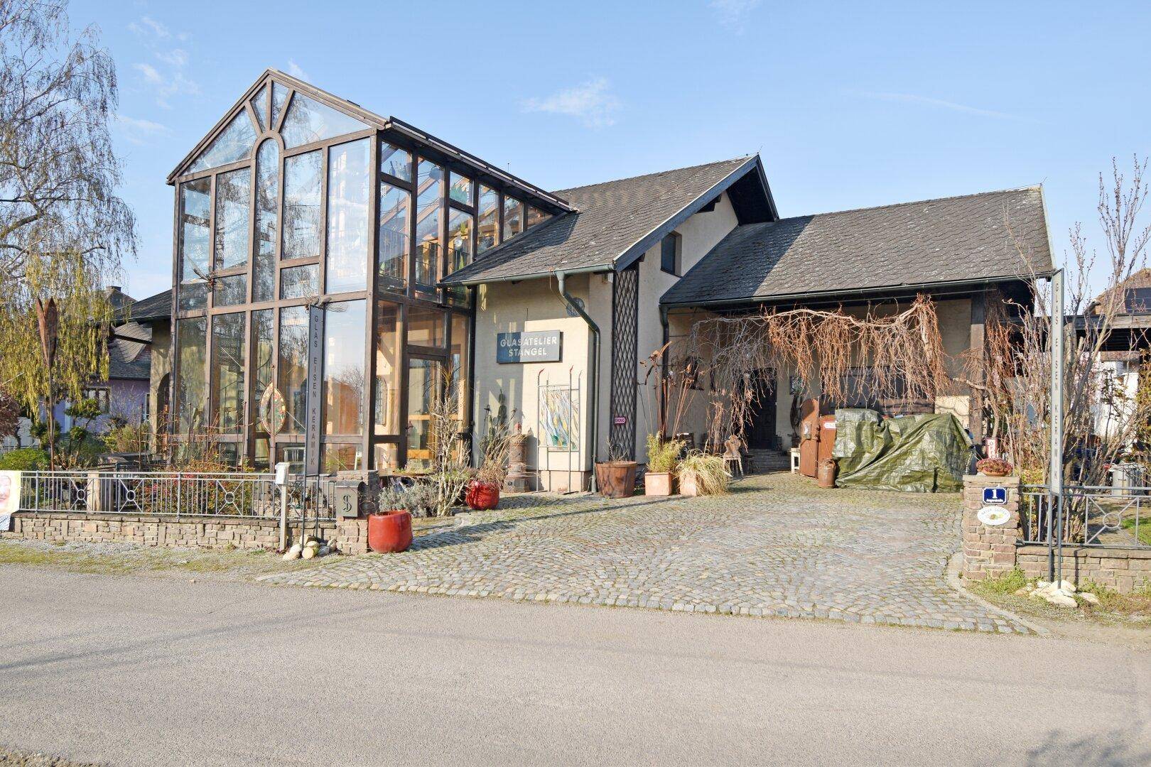 Ansicht des Hauses von der Straße mit großem Wintergarten und gepflasterter Einfahrt.