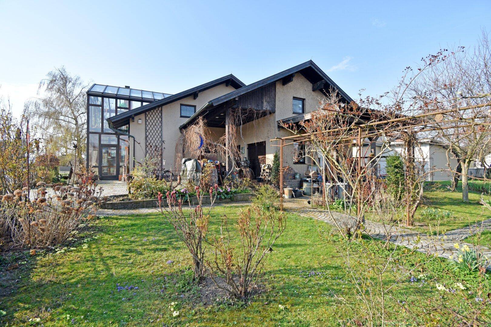 Weitläufiger Garten mit Rasenfläche, Bäumen und Blick auf das Haus mit Wintergarten.