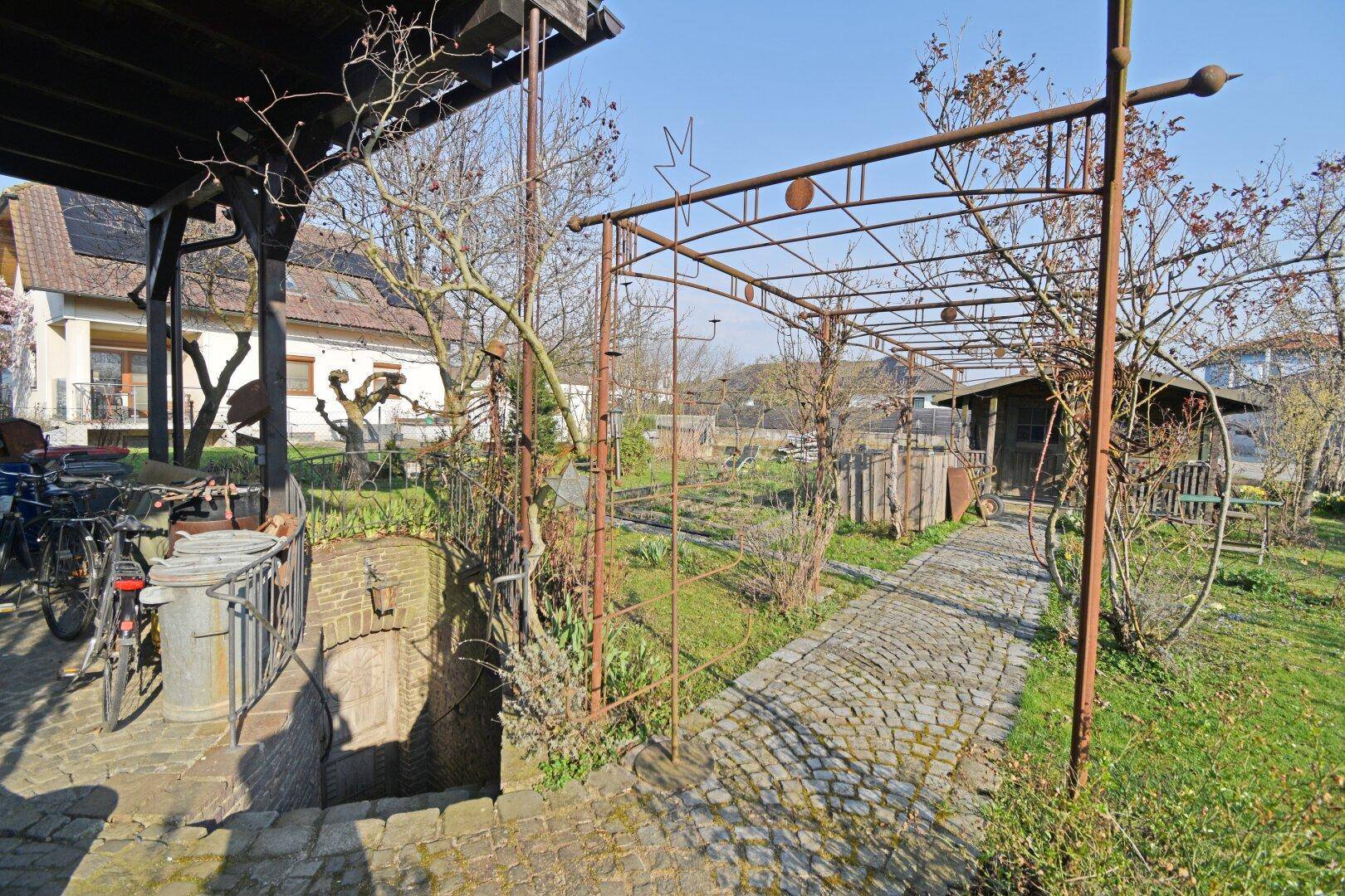 Gartenbereich mit Pergola, Kopfsteinpflasterweg und Zugang zum Keller.