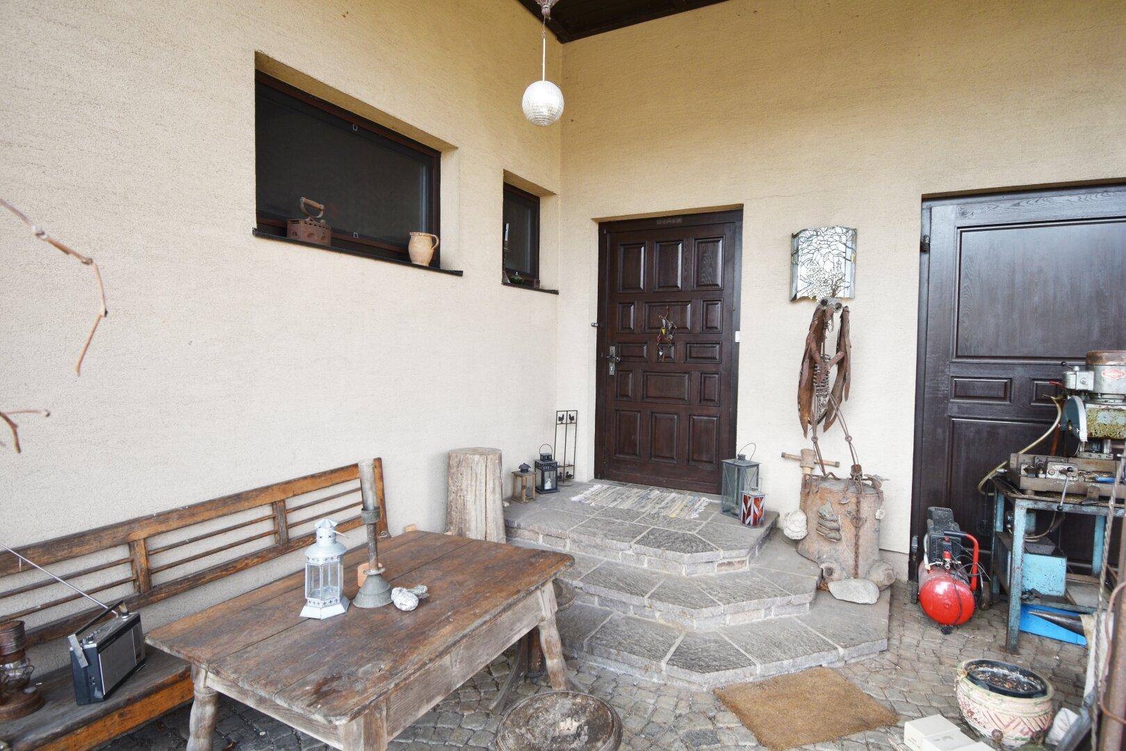 Überdachter Eingangsbereich mit Holztisch, Bank und rustikalen Dekorationen.