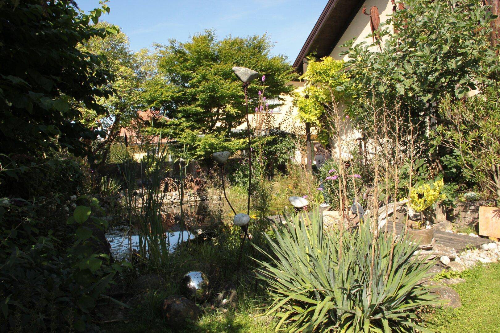 Idyllischer Gartenbereich mit Teich, üppiger Bepflanzung und dekorativen Elementen.