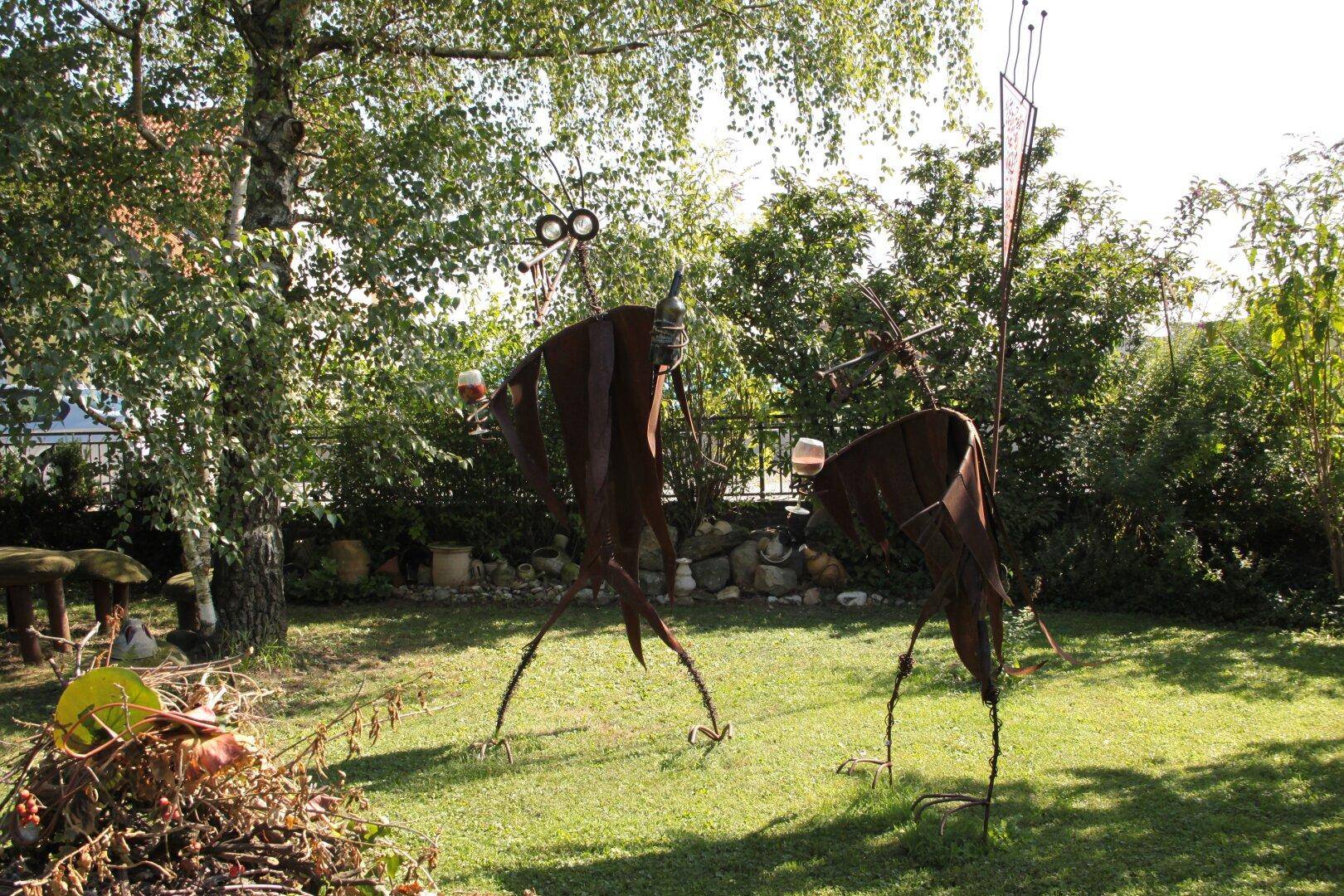 Grüne Rasenfläche im Garten mit dekorativen Metallskulpturen und Bäumen.