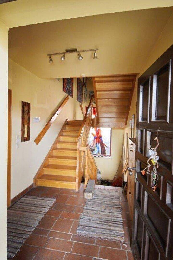 Eingangsbereich mit Holztreppe, Terrakottafliesen und dekorativen Wandbehängen.