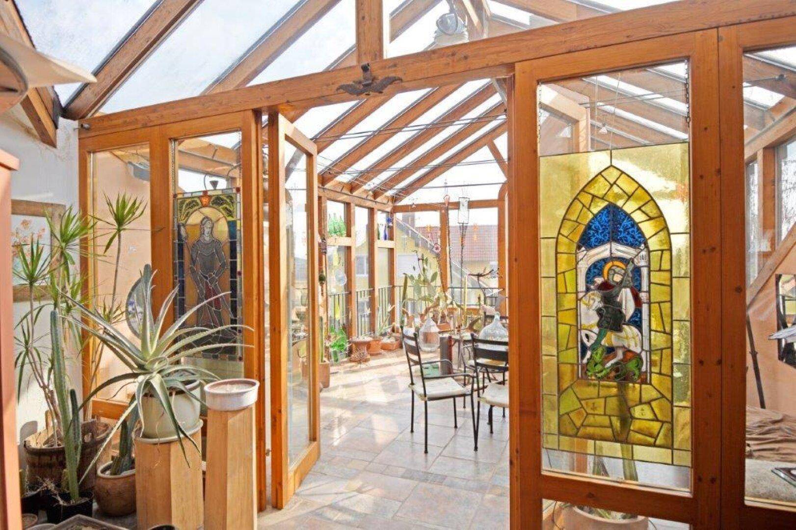 Heller Wintergarten mit Holzbalken, Buntglasfenstern und Pflanzen.