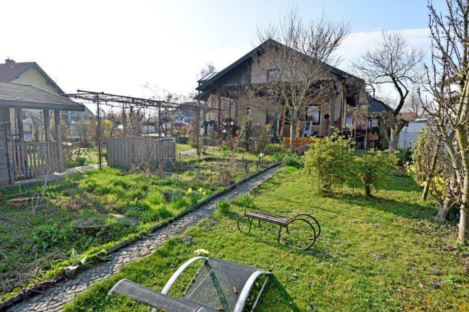 Weitläufiger Garten mit Rasenfläche, Gartenweg und Liegestuhl.
