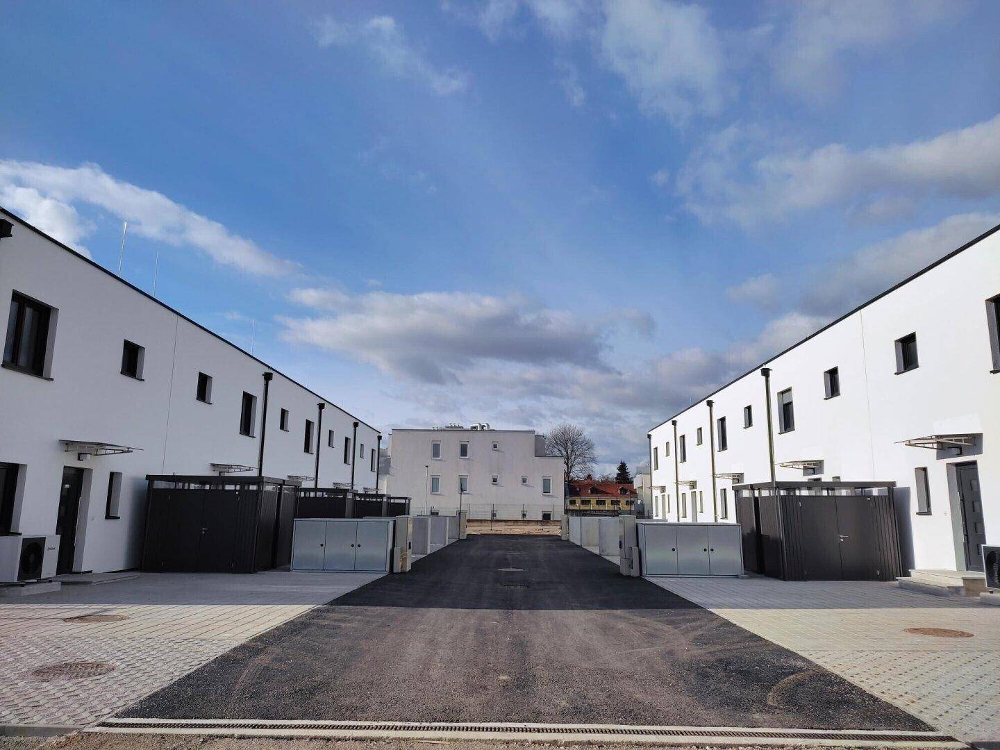 Zwei Reihen moderner Neubauten mit weißer Fassade und dunklen Akzenten unter blauem Himmel.