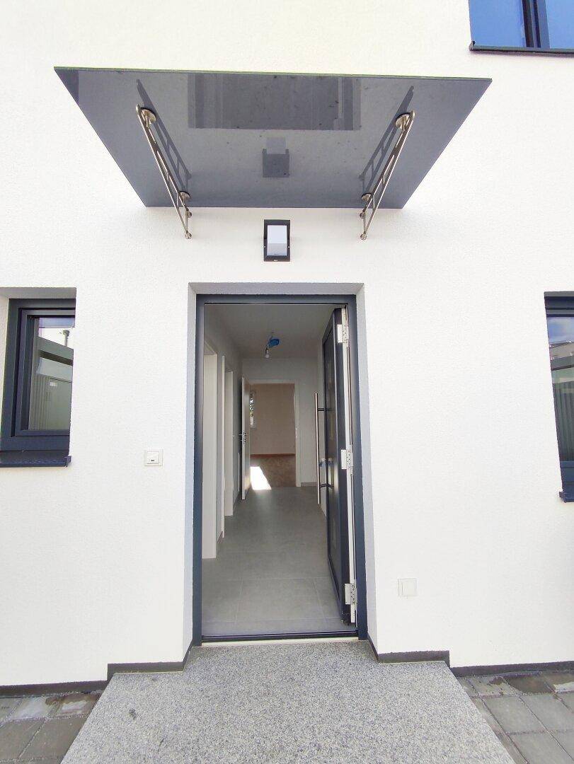 Eingangsbereich eines modernen Hauses mit offener Tür, die in einen hellen Flur führt.