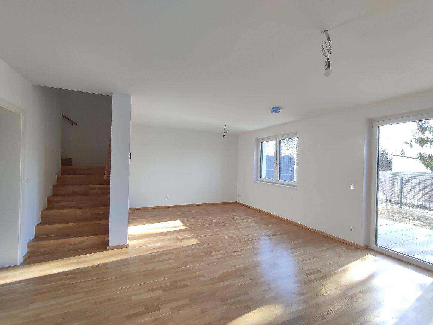 Heller Wohnbereich mit Holzfußboden, Treppenzugang und großer Terrassentür zum Außenbereich.