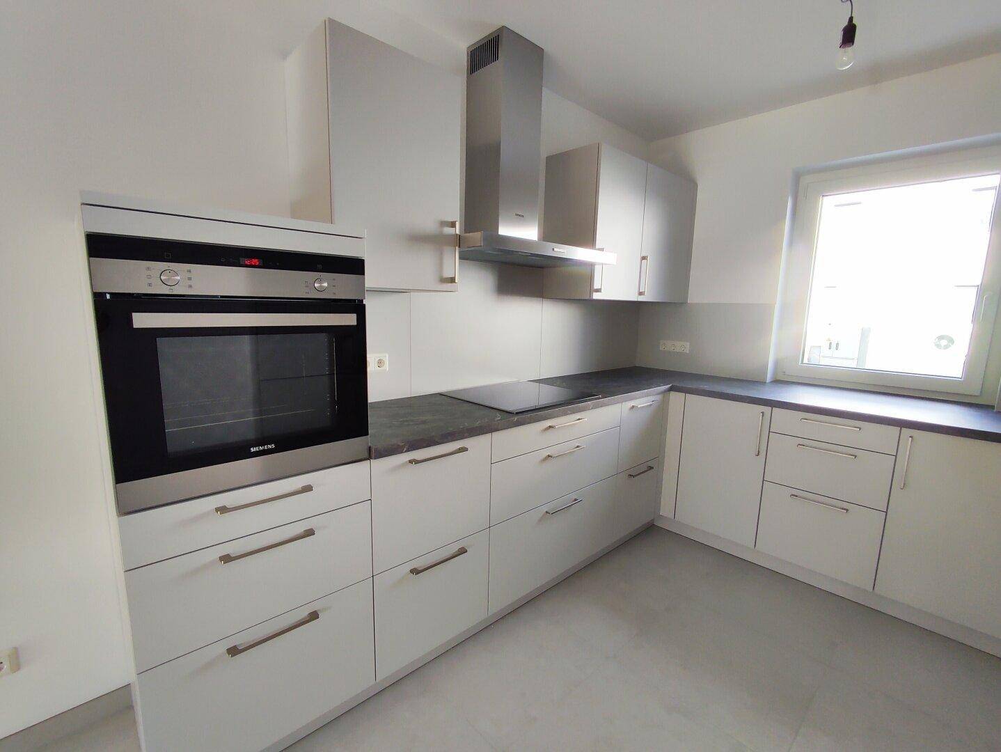 Helle Einbauküche mit modernen Geräten, Backofen auf Sichthöhe und Induktionskochfeld.