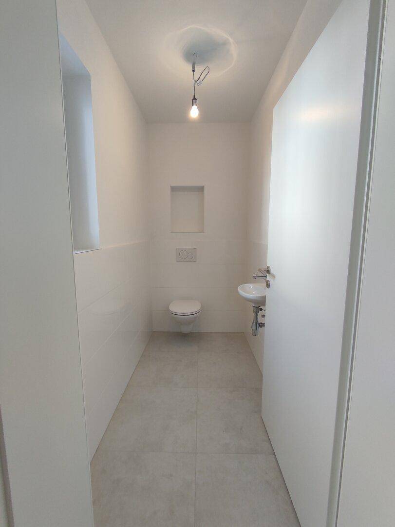 Modernes Gäste-WC mit wandhängender Toilette, kleinem Waschbecken und hellen Fliesen.