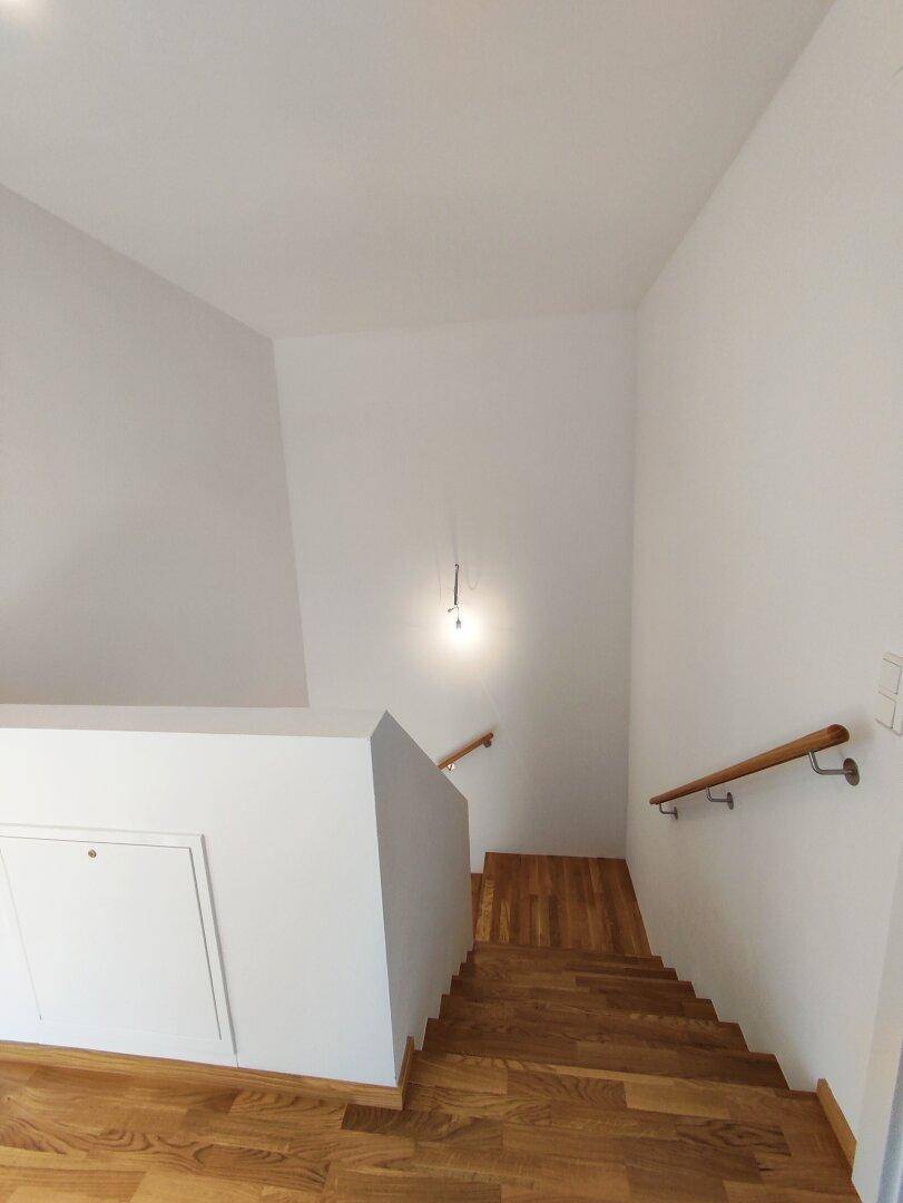Blick von oben auf die Holztreppe, die in die unteren Etagen führt, mit hellem Geländer.
